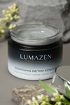 Open jar of Lumazen Soothing Detox Edelweiss Night Cream showing the light grey charcoal cream, on stone with alpine flowers