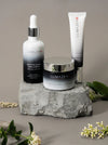 The Alpine Night Ritual set: Lumazen Edelweiss hair tonic, night cream and eye cream arranged on grey stone with alpine flowers